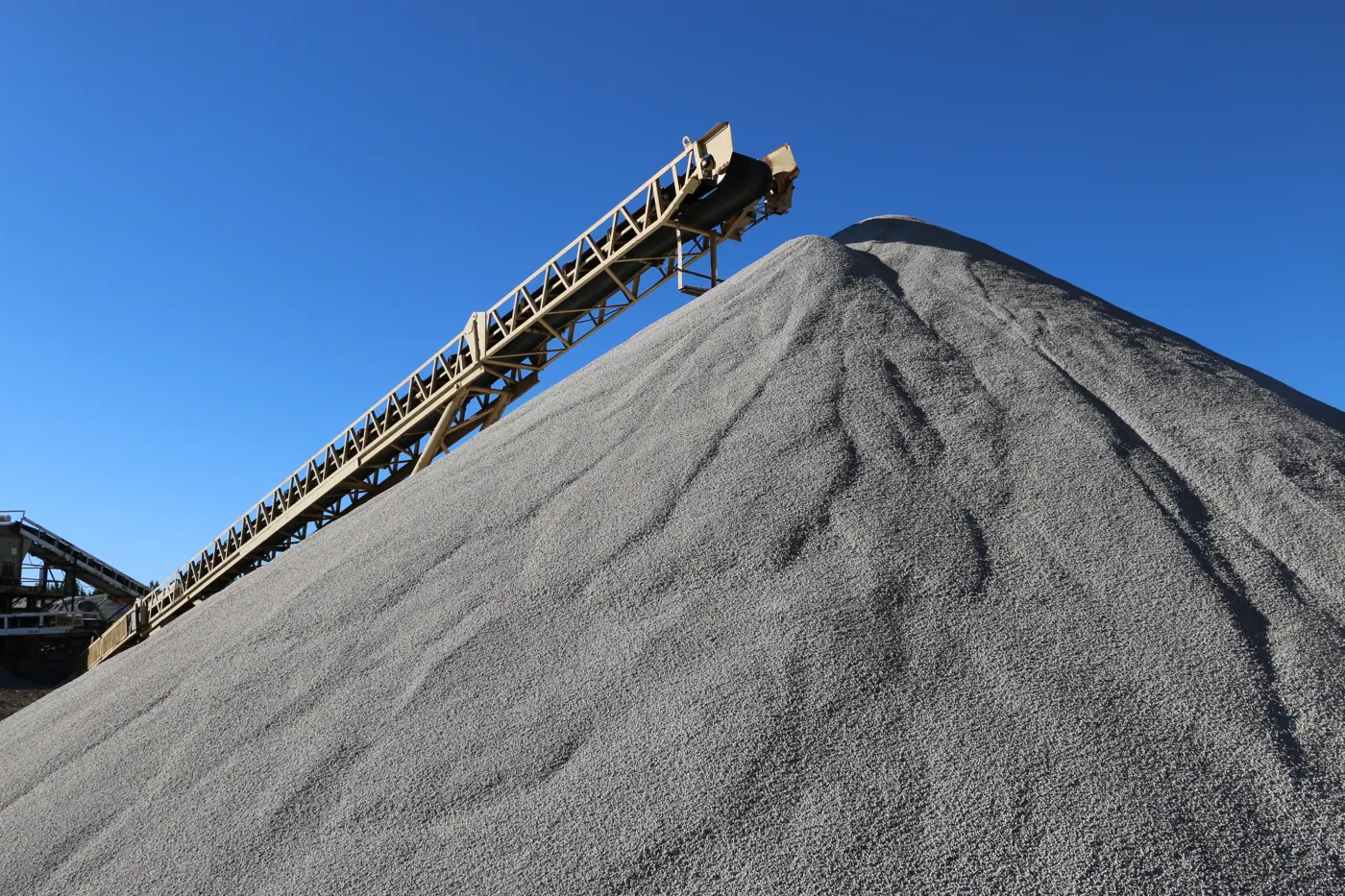 A stacker conveyor building a stockpile of screened pumice against a blue Oregon sky