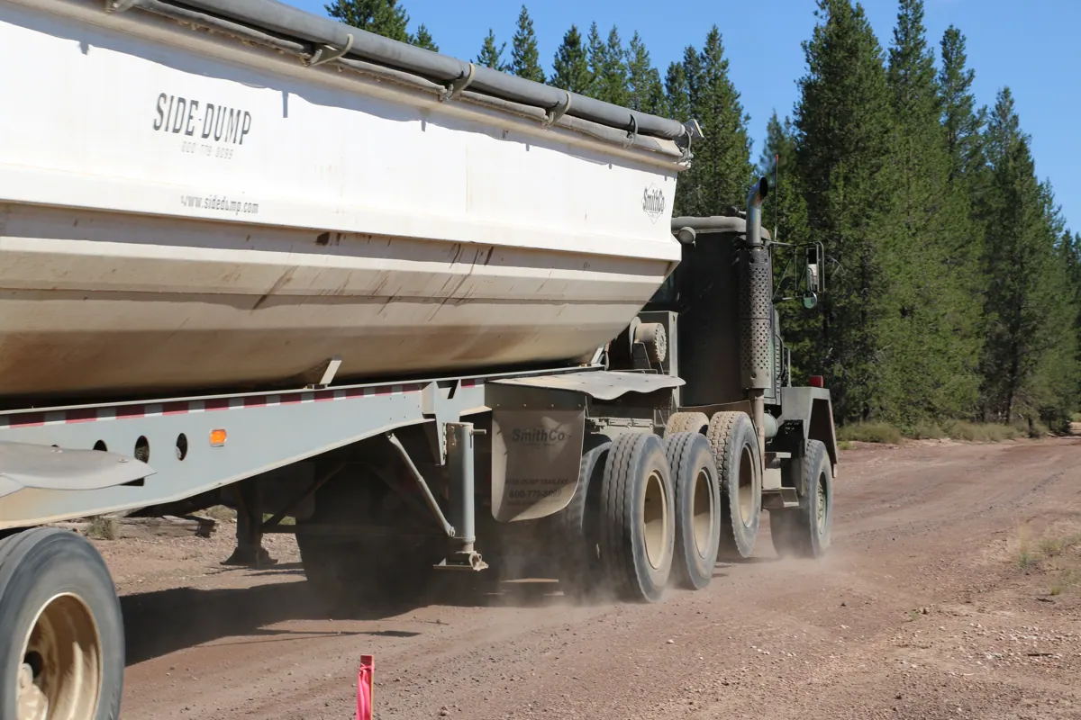 A high-capacity side-dump trailer hauling Beaver Pumice down a forest road